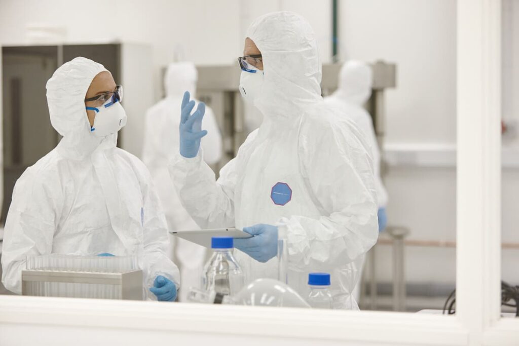 Two gowned operators discussing process data on a tablet inside a cell and gene therapy cleanroom